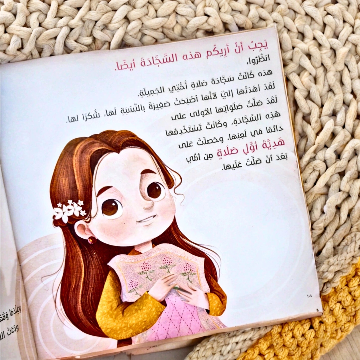 Sajadati Al Jameela Arabic children's book displayed on a beautifully patterned prayer mat. The book cover features an illustrated girl holding a colorful patchwork prayer mat, emphasizing the story’s theme of faith and prayer for young Muslim kids