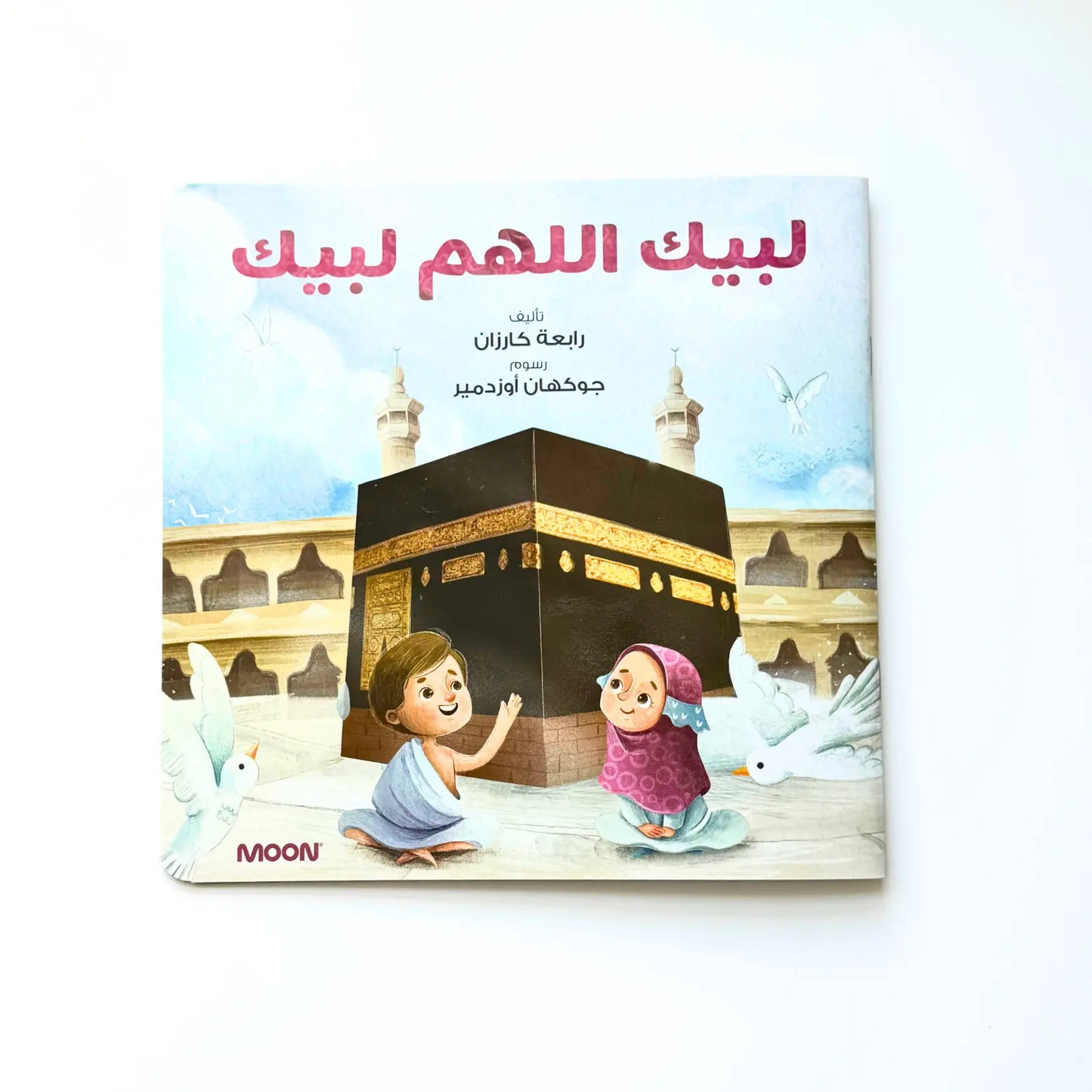 A happy family sitting on a rug, looking at a picture of the Kaaba with shining eyes and big smiles
